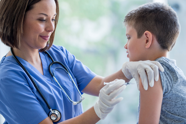 A nurse is giving a elementary age boy a flu shot at the doctor's office.